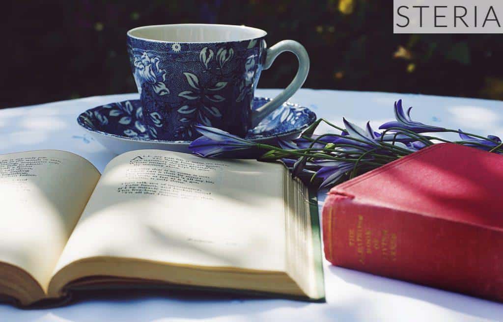 Book Opened on Top of White Table Beside Closed Red Book and Round Blue Foliage Ceramic Cup on Top of Saucer