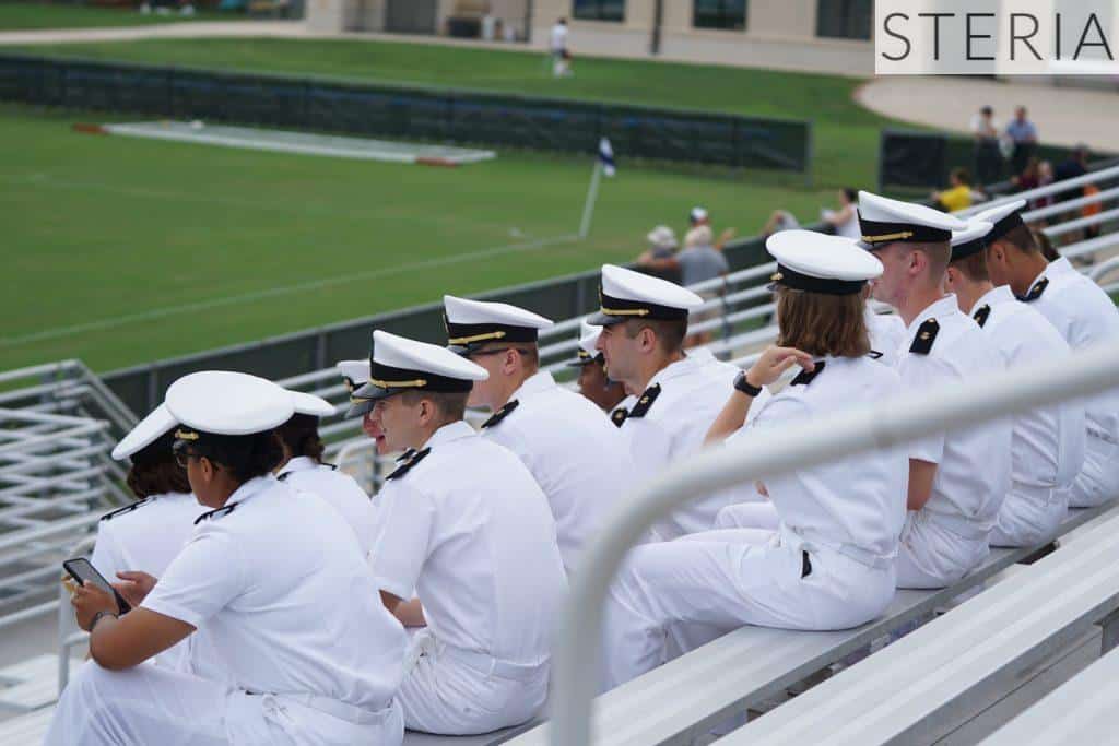 group of people in white uniform sitting looking at field during daytime